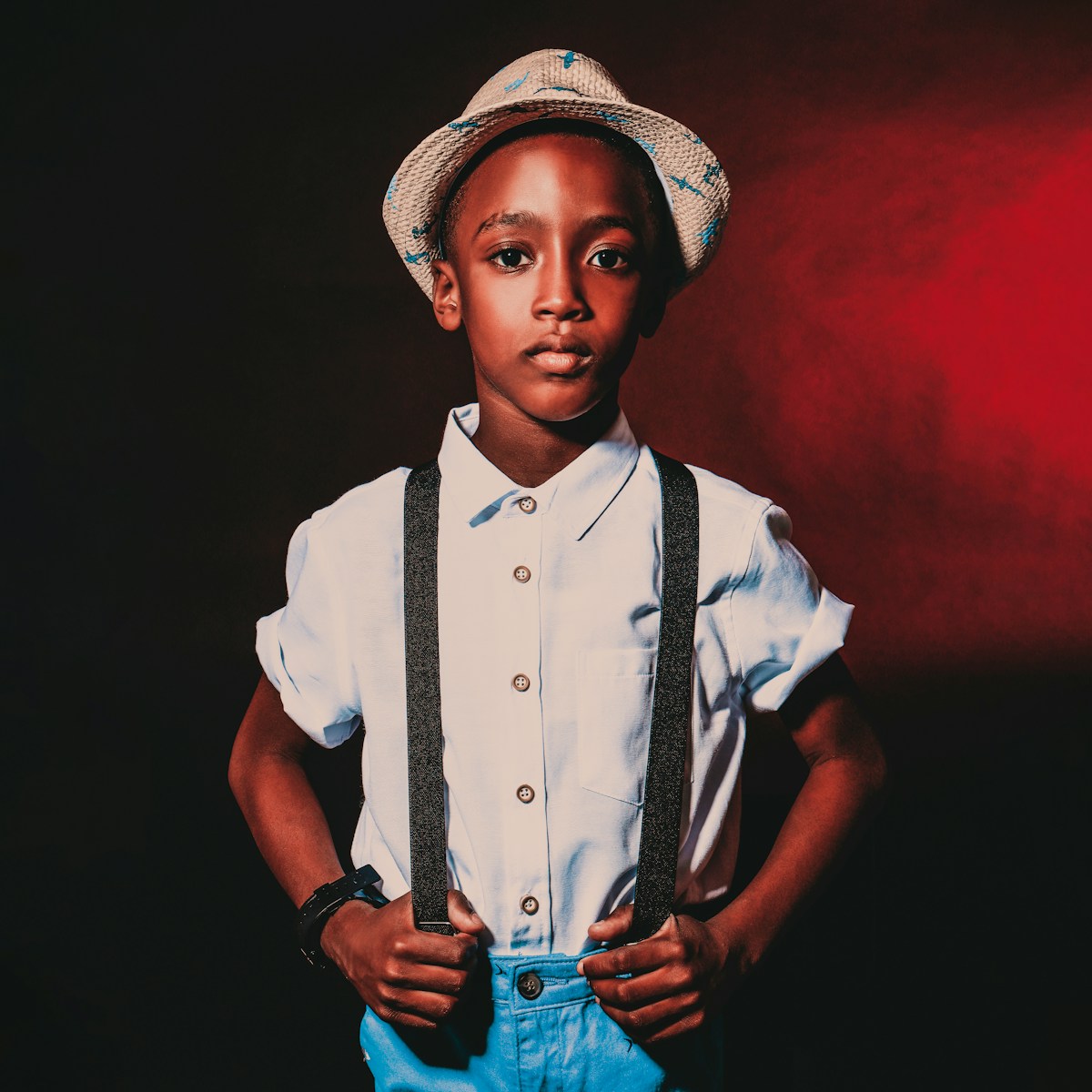 a young boy wearing suspenders and a hat